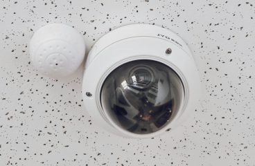 Close-up of a round dome surveillance camera installed on a speckled ceiling for security monitoring.
